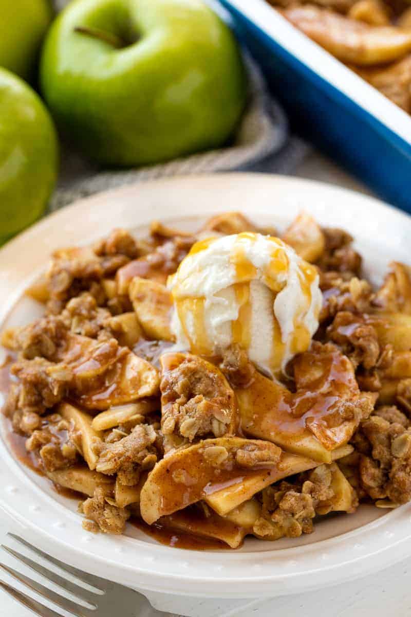 The Best Ever Apple Crisp has a juicy caramel filling and topped with the perfect blend of sugary crumble on top. Eat it warm with a scoop of vanilla ice cream for an amazing dessert! Apple Crisp served up on a white plate topped with a scoop of ice cream and caramel.