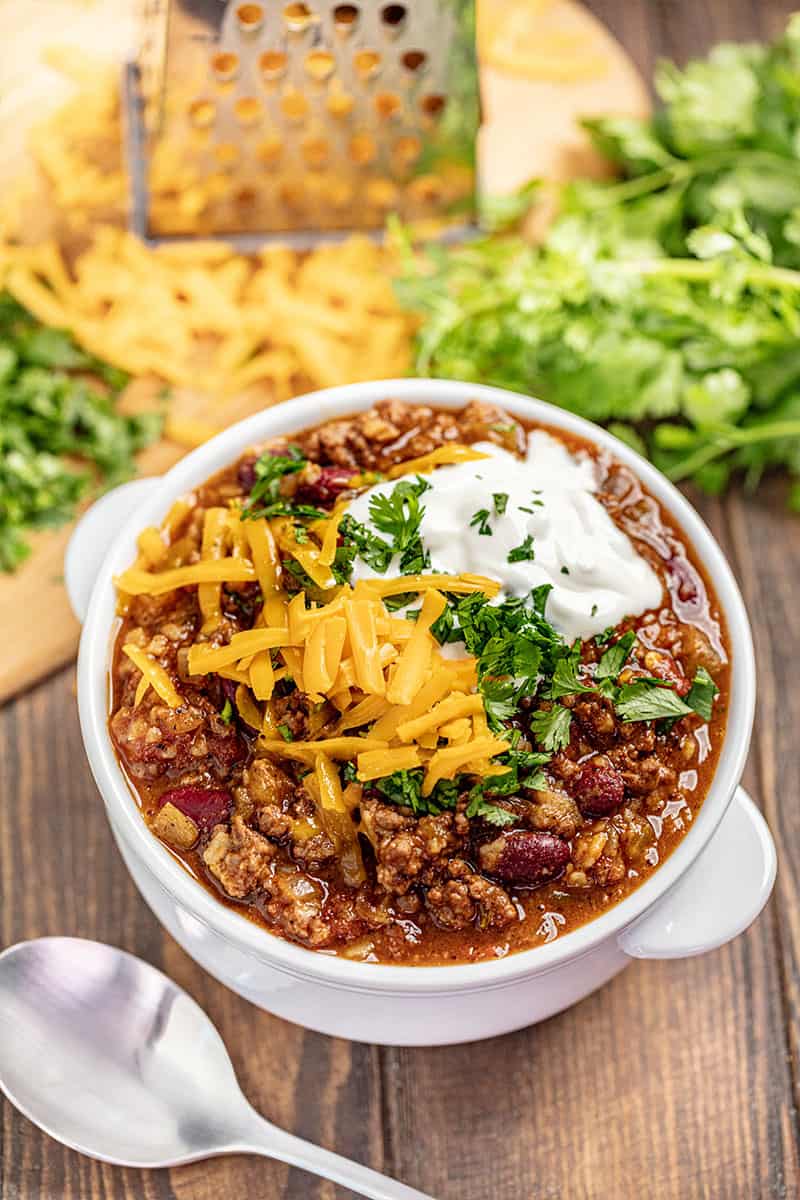 This easy chili recipe is the best! It is full of flavor and satisfying, hearty beans and beef. Perfect for fall and the days when a warm bowl of chili is just what the doctor ordered. Bird's eye view of Chili topped with parsley cheese and sour cream in a white bowl.