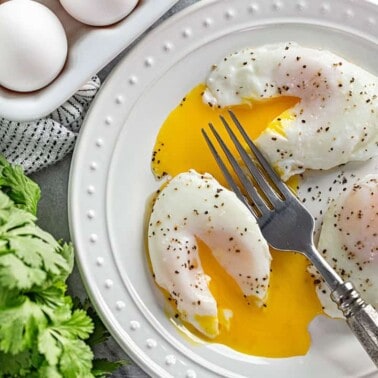 A bird's eye view of Poached Eggs, seasoned with salt and pepper, with runny yolks after being cut into with a fork.