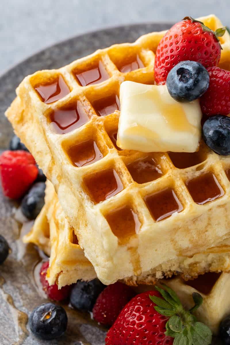Making homemade waffles has never been easier! This waffle recipe is fail proof and can be made ahead and kept in the fridge for up to 5 days. It makes a perfect waffle that is fluffy on the inside and crispy on the outside. Close up, overhead view of a stack of homemade waffles with a pat of butter and fresh berries on top.