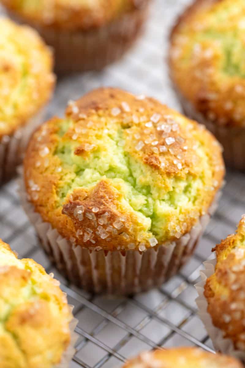 These Pistachio Muffins taste like they came from a bakery with their perfectly domed tops and delicious pistachio flavor. Angled photo of Pistachio Muffins on a wire rack.