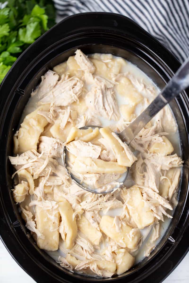 This Crockpot Chicken and Dumplings Recipe is easy to make and full of old fashioned goodness with delicious flat rolled dumplings made from scratch. Bird's eye view of a ladle full of Chicken and Dumplings in a slow cooker.
