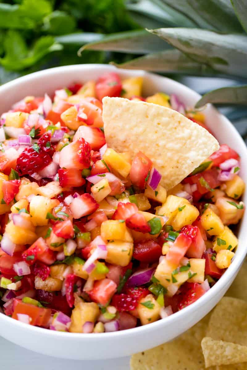Strawberry Pineapple Salsa will have everyone raving at your next party! People love the fresh, fruity zing from this tasty fruit salsa! A tortilla chip dips into a bowl of Strawberry Pineapple Salsa