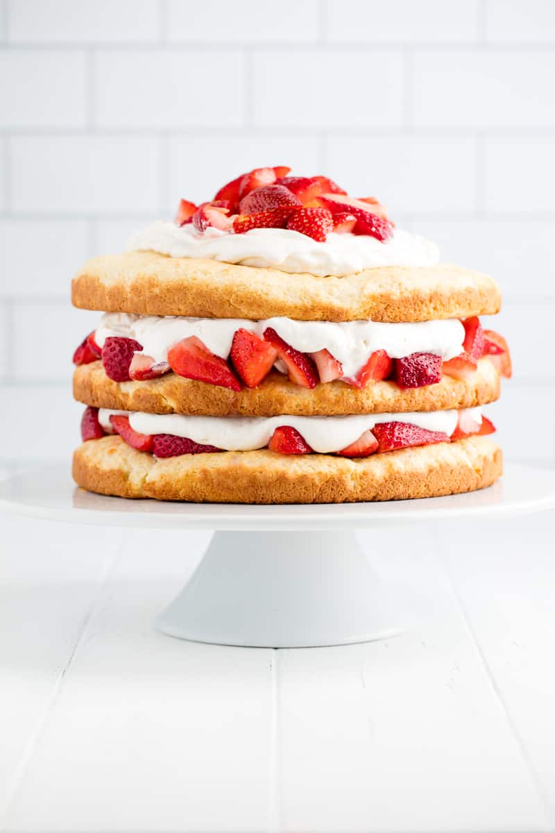 Strawberry Shortcake is a classic dessert that is perfect for spring and summer. This three layer strawberry dessert is not only beautiful, it's also delicious! Strawberry Shortcake on a white cake stand.