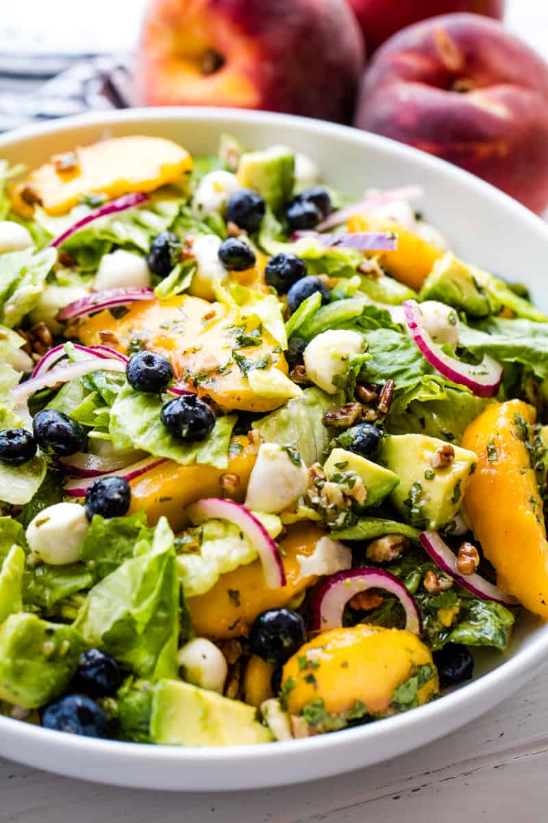 Meet your new favorite salad! Summer Peach Salad is full of the sweet flavors of late summer with peach, blueberry, avocado, mint, mozzarella and more! Peach Salad in a white bowl.