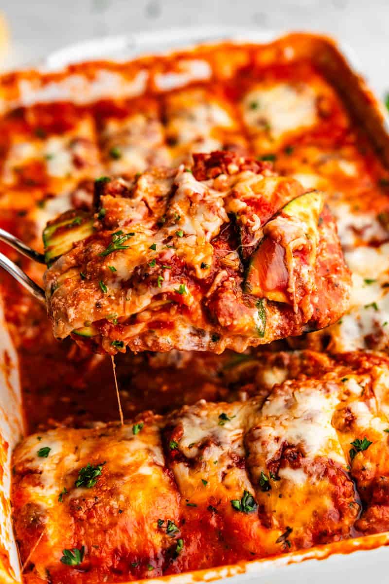 A close up of a square of zucchini lasagna being lifted from the casserole pan.
